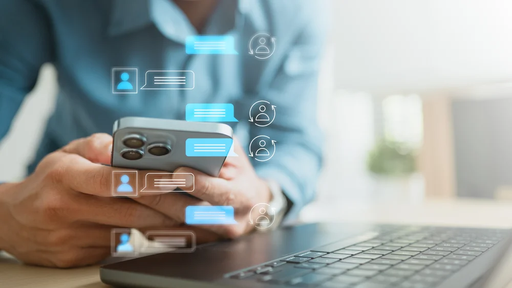 Person using a smartphone with AI chat conversation bubbles and contact icons floating above, illustrating how businesses appear in AI assistant answers - 4D Digital AI Visibility
