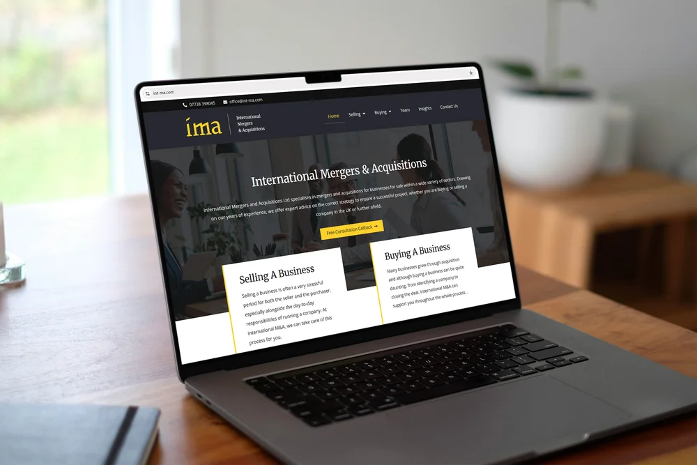 IMA 'International Mergers & Acquisitions' homepage shown on a MacBook on a desk
