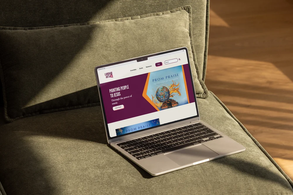 Langham Arts homepage shown on a MacBook resting on a sofa